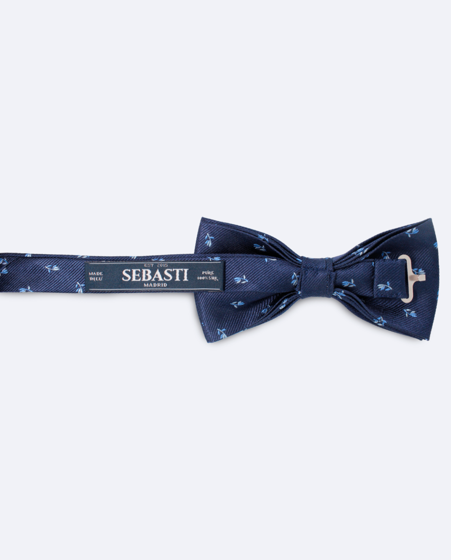 Vista trasera de la pajarita en seda azul marino con diseño de flores azul claro, con cinta ajustable y marca Sebasti en la etiqueta