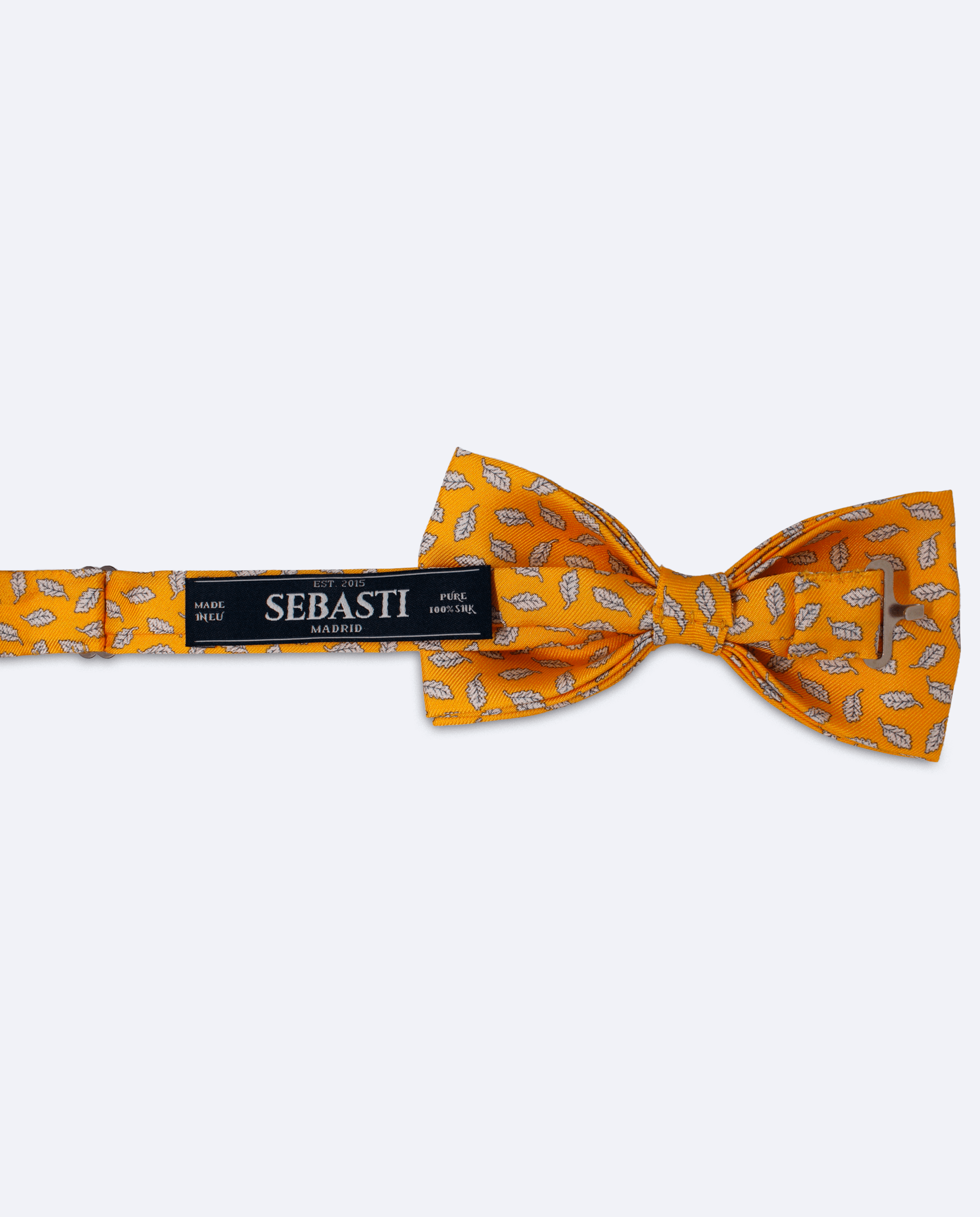 Vista trasera de la pajarita mostaza con hojas blancas de seda. Incluye cinta ajustable y marca Sebasti en la etiqueta