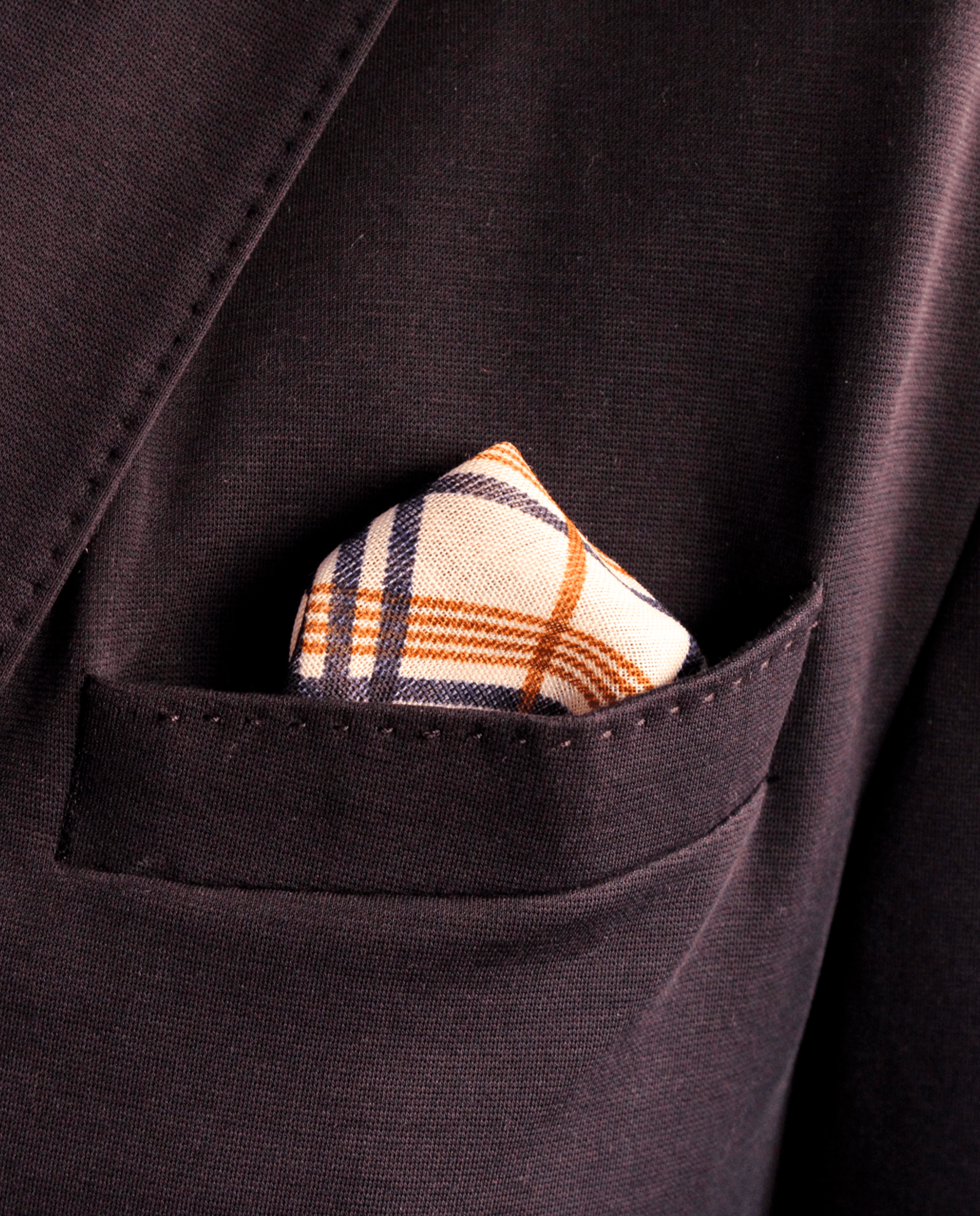 Pañuelo de bolsillo beige con cuadros azul marino y marrón, colocado en el bolsillo de una americana | Sebasti