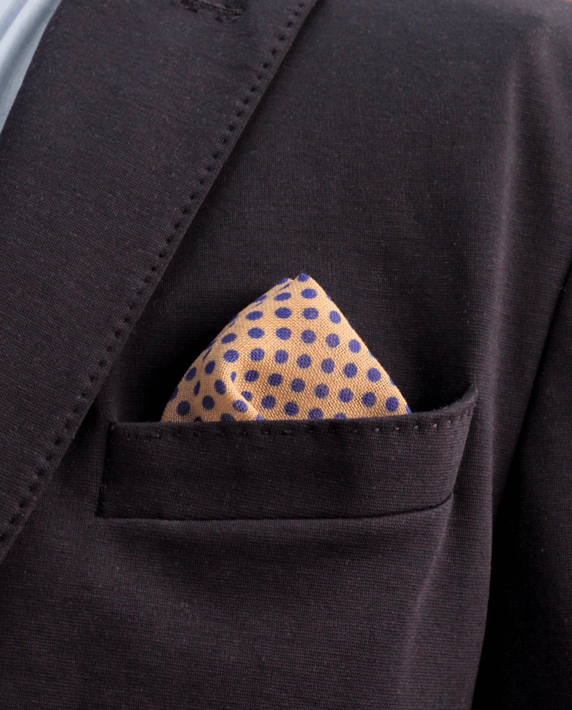 Pañuelo de bolsillo beige crema con lunares azul marino, colocado en el bolsillo de una americana | Sebasti