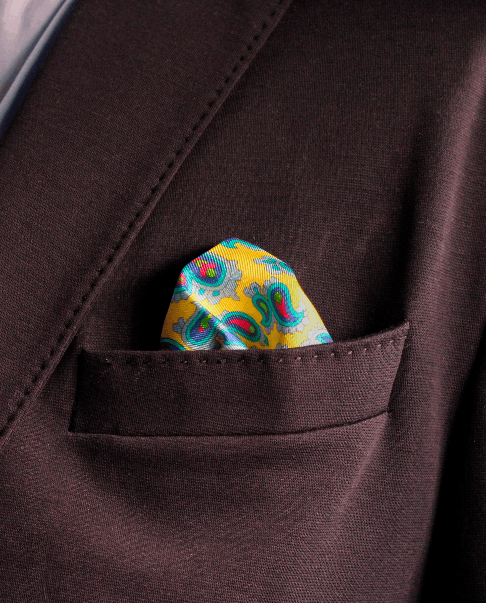Pañuelo de bolsillo de seda amarillo con paisley multicolor, colocado en el bolsillo de una americana | Sebasti